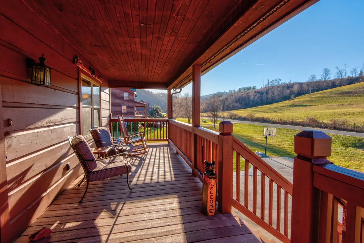 The front porch is furnished with classic rocking chairs and offers panoramic views of rolling hills. The welcoming sign and porch details create a sense of arrival, while the scene invites relaxation, morning coffee, and casual conversations while observing the outdoors.