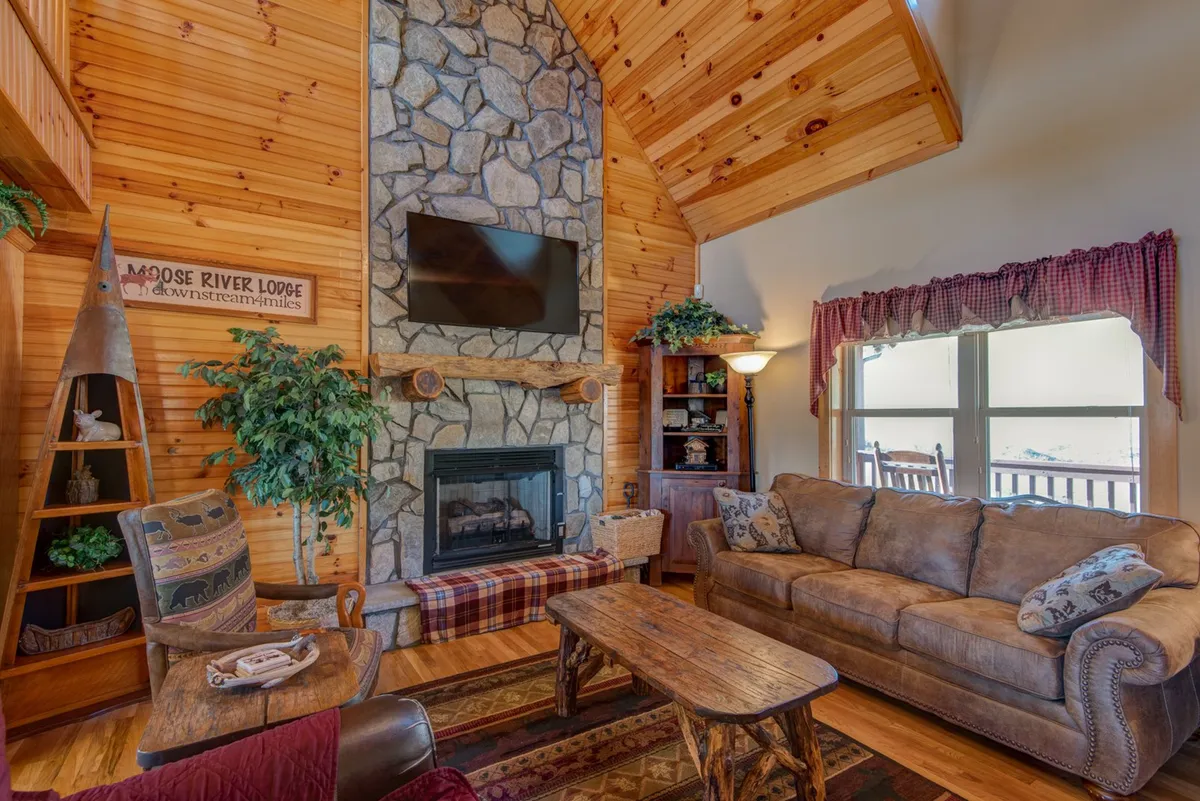 A cozy living area centered around a stone fireplace, with a comfortable couch, decorative pillows, a wooden coffee table, and large windows revealing scenic outdoor views. The ambiance is warm and welcoming, perfect for family gatherings or relaxing evenings.