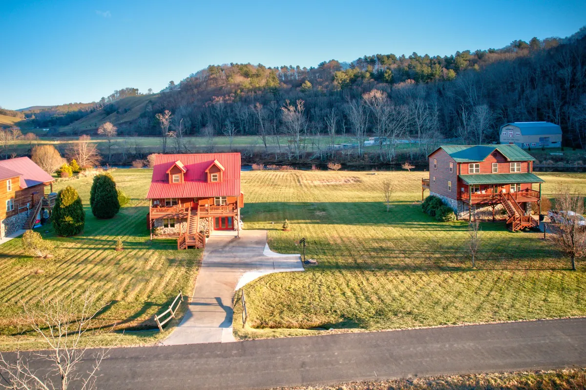 The image shows charming log cabins set on a manicured lawn with a scenic mountain backdrop. The expansive outdoor area invites guests to enjoy sunsets, stargazing, or group activities like barbecues and nature walks.