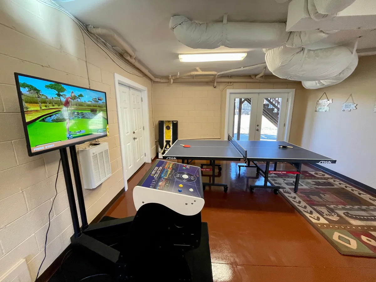 A recreational room showcasing a ping pong table, classic arcade machine, and a television, all set in a bright, inviting environment. The focus on gaming and relaxed fun is clear.