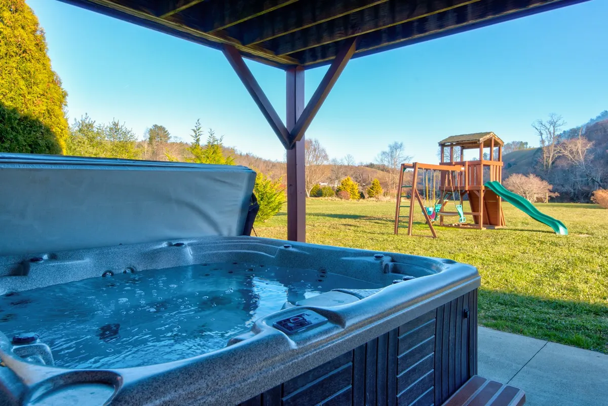 An exterior space featuring a large hot tub, children's playground equipment, and lush green surroundings. The mood is cheerful and welcoming, ideal for both relaxation and outdoor play.