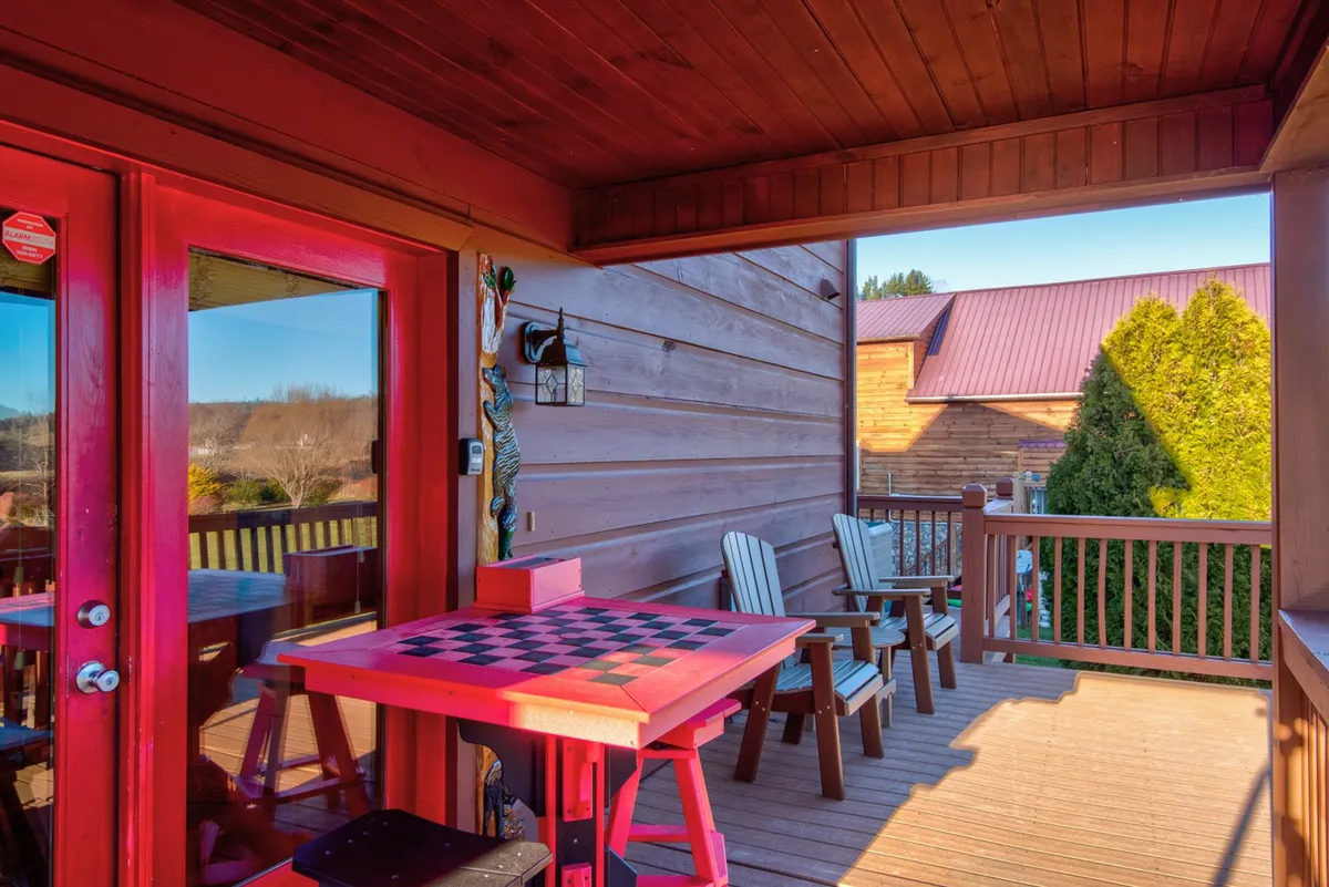 An exterior porch scene with red doors, a checkered table, wooden chairs, and a decorative lantern. The setting suggests socializing or enjoying meals outdoors, with views extending to the surrounding landscape. The casual yet romantic ambiance evokes evenings spent sipping wine or playing games, set against a backdrop of nature.